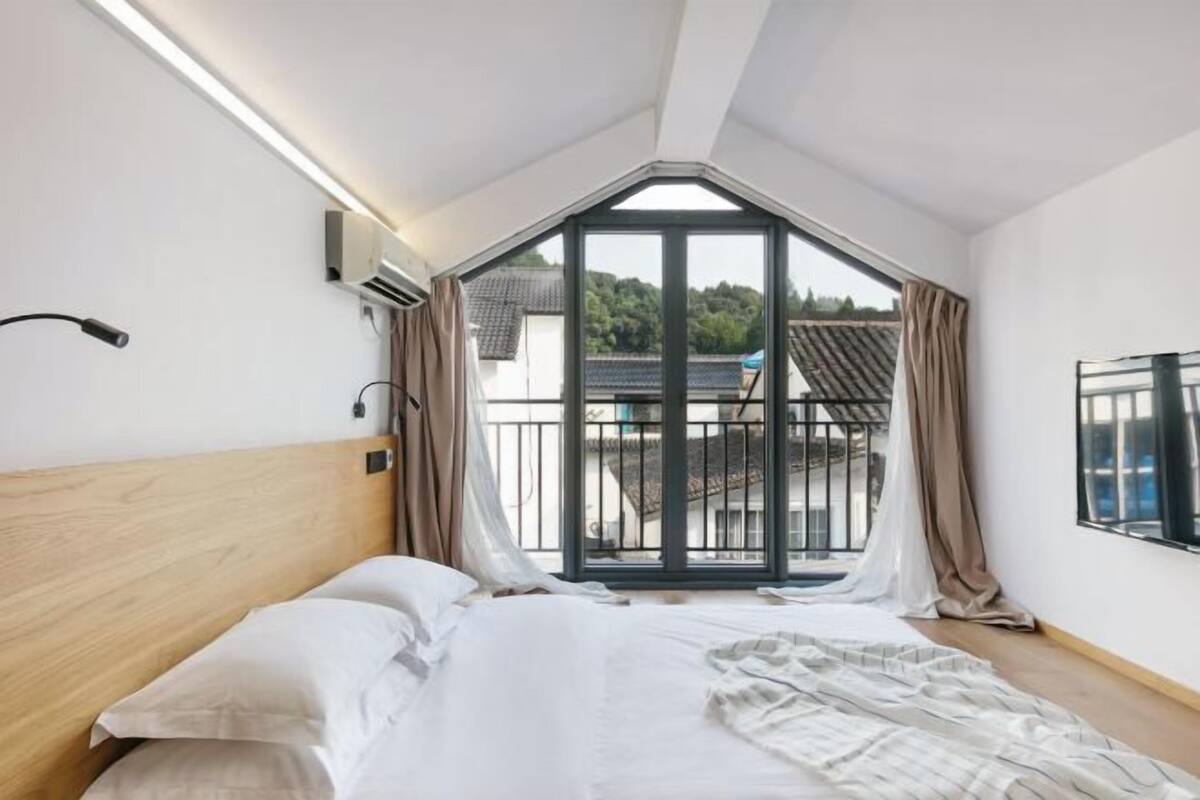 Ein Schlafzimmer mit großem Fenster, einem Bett und Blick auf ein Gebäude.