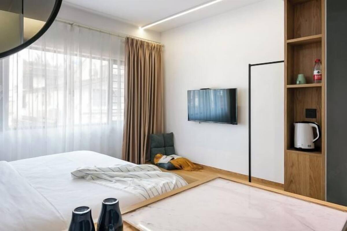 Ein modernes Hotelzimmer mit Bett, Flachbildfernseher, einem Holzbodenregal mit Wasserkocher und Blick nach außen.