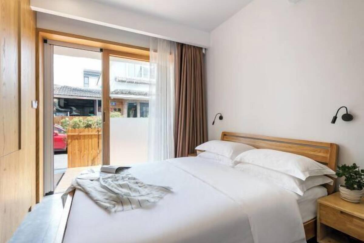 Ein Hotelzimmer mit Bett, Holz-Kopfteil, Nachttisch, Topfpflanze und Blick nach draußen.