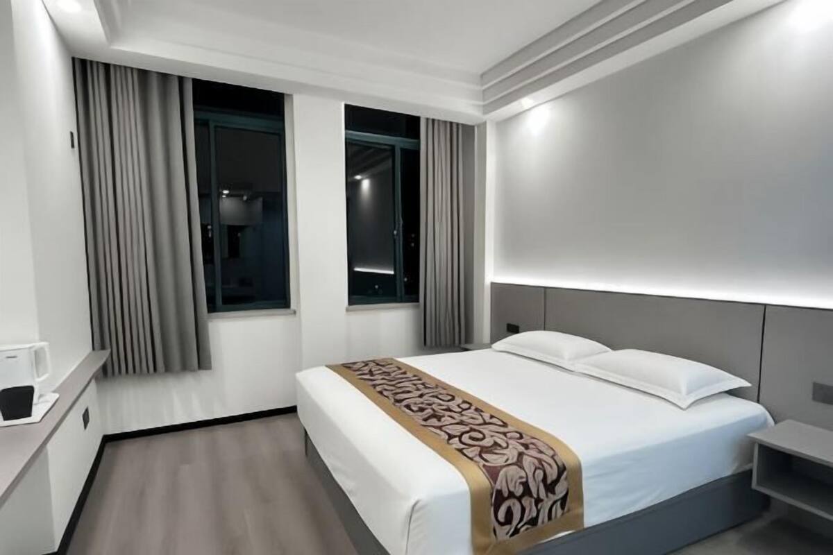 A hotel room with a bed, bedside table, and a window with curtains.