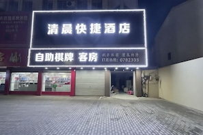 L’entrée d’un hôtel, avec une enseigne au néon, un auvent rouge et un trottoir pavé.