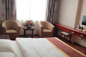 A hotel room with a bed, two armchairs, a small table with a vase of flowers, a desk, and a television. - Qingcheng Express Hotel (Ma'anshan)
