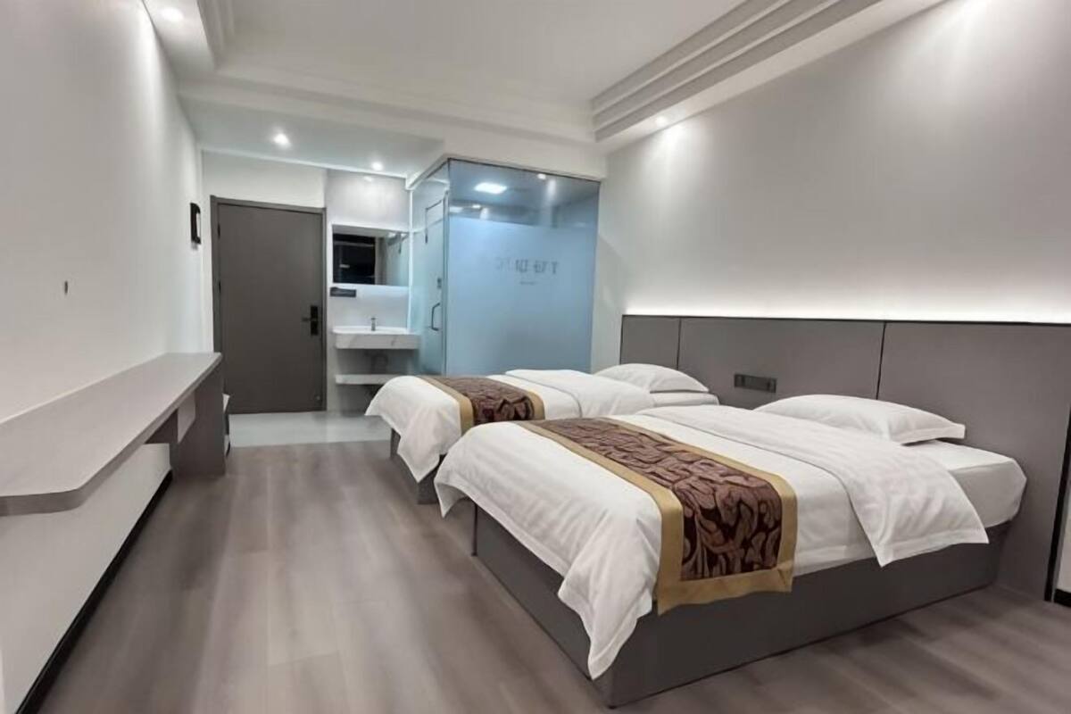 A modern hotel room with a large bed, a bedside table, a mirror, and a bathroom visible in the background.