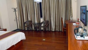 A hotel room with a bed, a desk with a chair, a television, and a window with curtains. - Tianyue Business Hotel (Haikou)