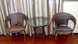 Two wicker chairs and a glass table in a room with wooden flooring and a curtain backdrop. - Tianyue Business Hotel (Haikou)