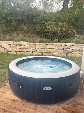 Un jacuzzi con un muro de piedra y follaje al fondo.