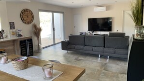 Een moderne woonkamer met een grijze bank, een flatscreen televisie, een houten eettafel met kaarsen en een grote wandklok.