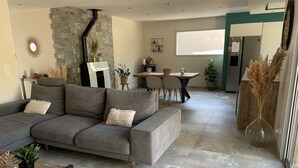 Een moderne woonkamer met een grijze modulaire bank, een accentmuur van steen, en een eethoek met een tafel en stoelen.