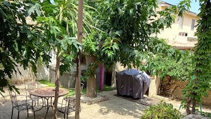 Uma área de pátio com pérgola, móveis de exterior e espaço coberto para churrasco.