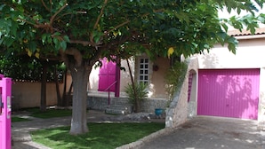 Uma área residencial com uma garagem rosa, uma árvore e um gramado bem cuidado.