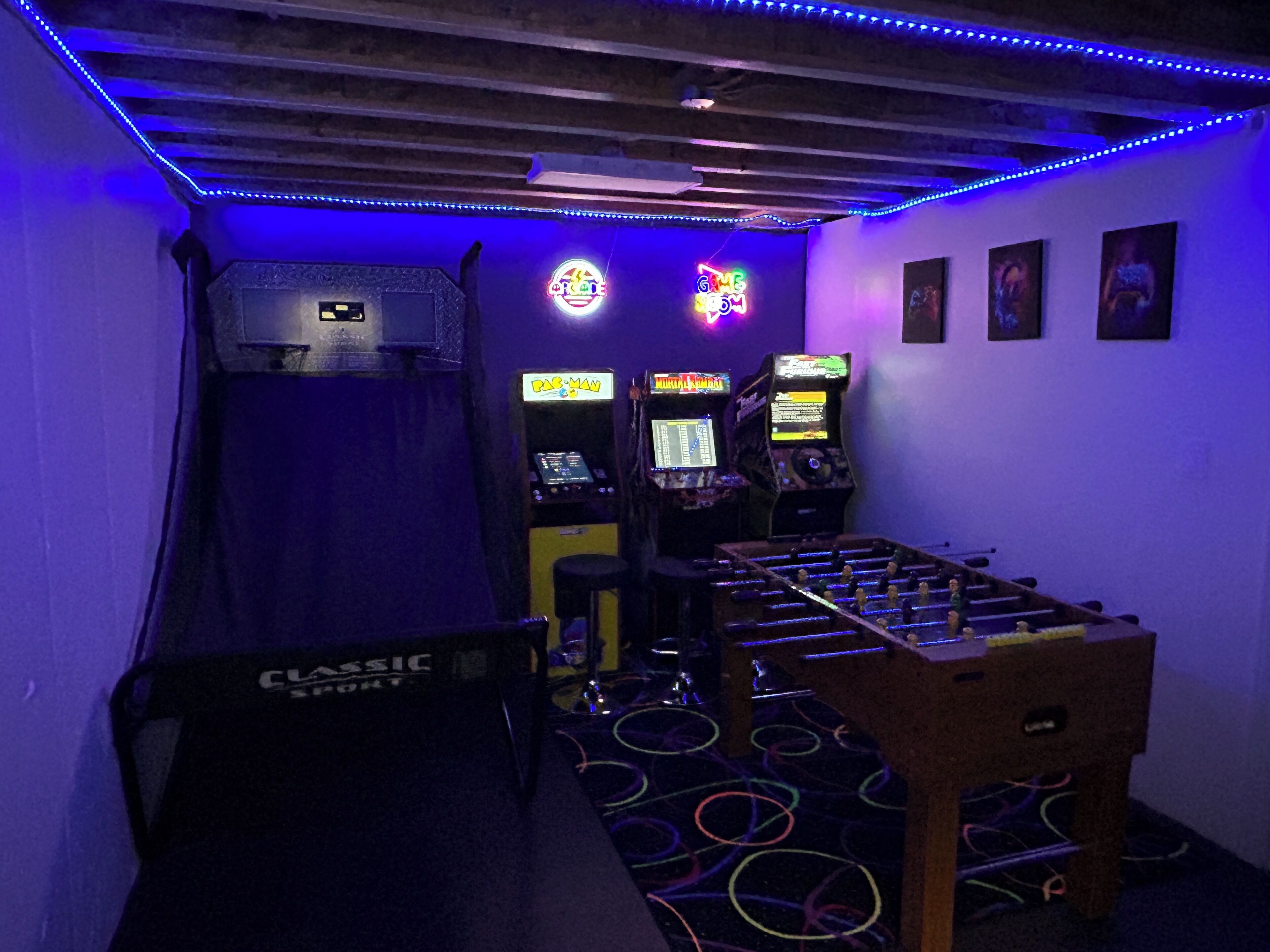 Una habitació amb taula de futbolí, jocs arcade i un cartell de neó.