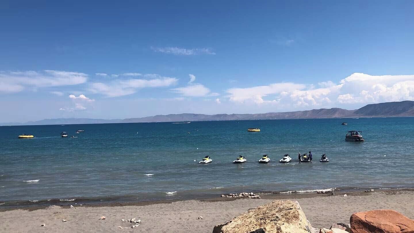 Una playa con cielo despejado, mar tranquilo y montañas a lo lejos.