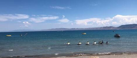 Una playa con cielo despejado, mar tranquilo y montañas a lo lejos.