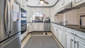 Une cuisine moderne avec des meubles blancs, des appareils en acier inoxydable, un ventilateur de plafond et un tapis à motifs.