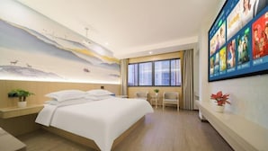 A hotel room with a large bed, a mural on the wall, a TV screen displaying movie posters, and a small table with chairs. - Pujiang Qianbaidu Hotel (Pujiang)
