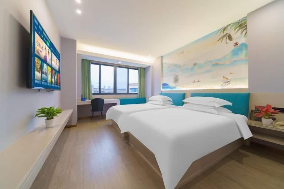 A hotel room with a large bed, a desk, a TV mounted on the wall, and a painting of a beach scene.