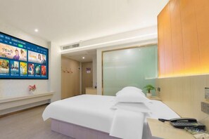 Una habitación de hotel con una cama, un televisor montado en la pared, un escritorio con un teléfono y una partición de vidrio.