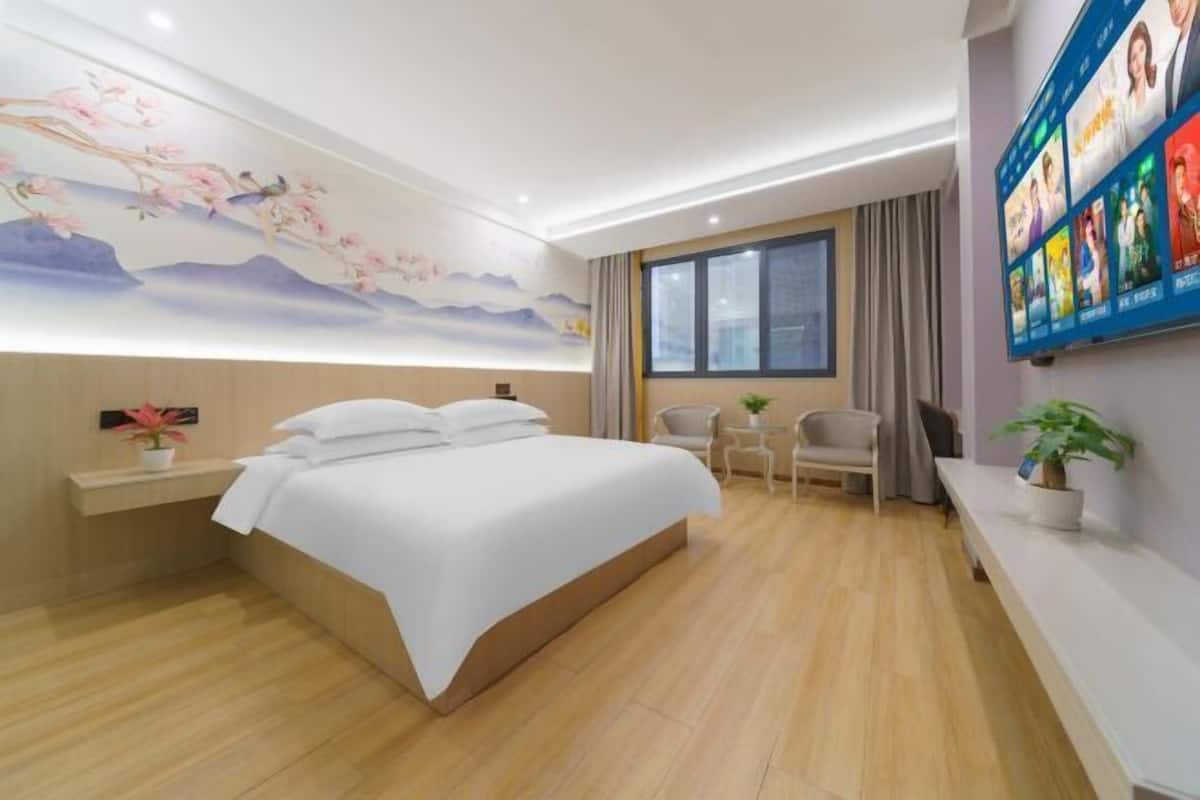 A hotel room with a large bed, a desk, a chair, a TV, and a wall with a floral mural.