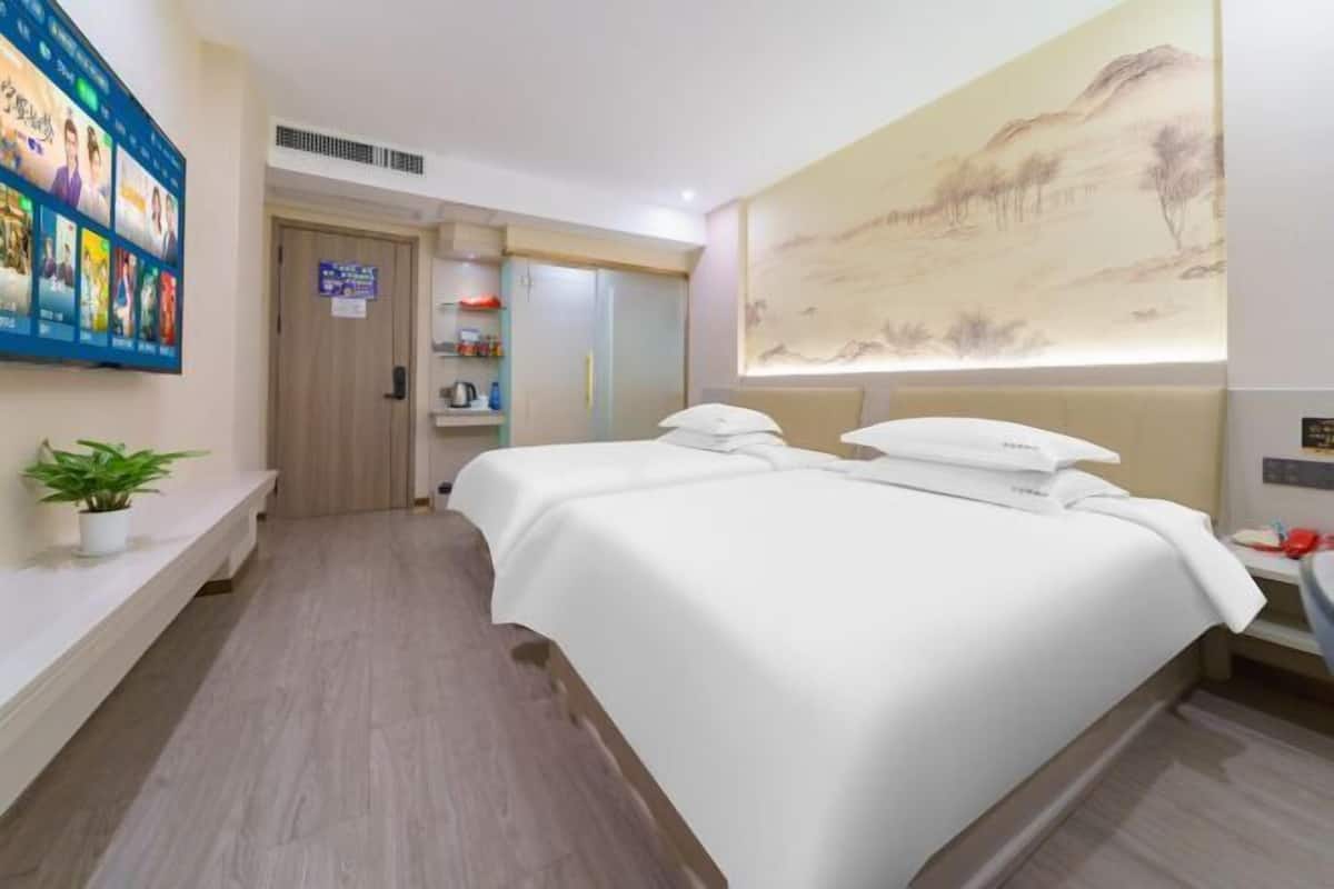 A hotel room with a large bed, a wall-mounted TV, a painting, and a shelf with toiletries.