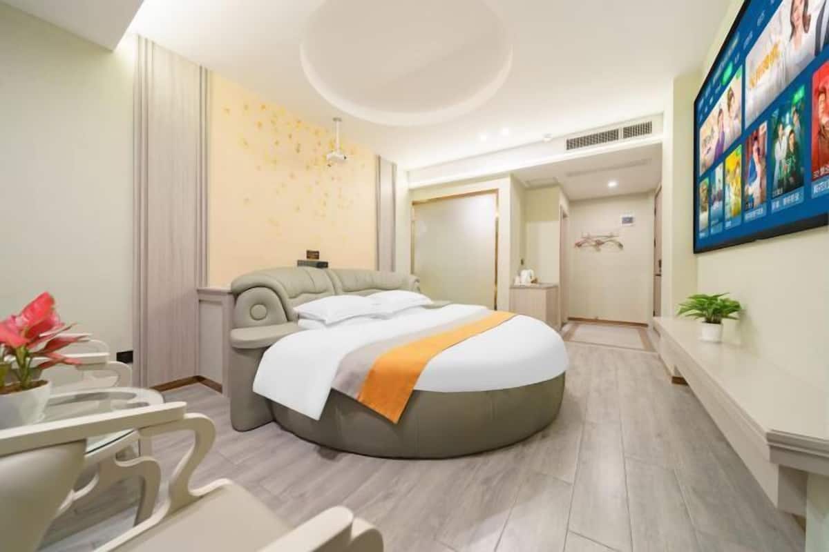 A modern hotel room with a round bed, a small desk, and a television mounted on the wall.