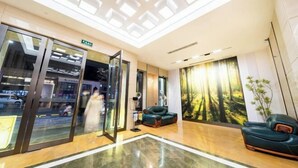 A modern lobby with a glass door entrance, a seating area with a sofa and a chair, and a large forest-themed mural on the wall. - Pujiang Qianbaidu Hotel (Pujiang)