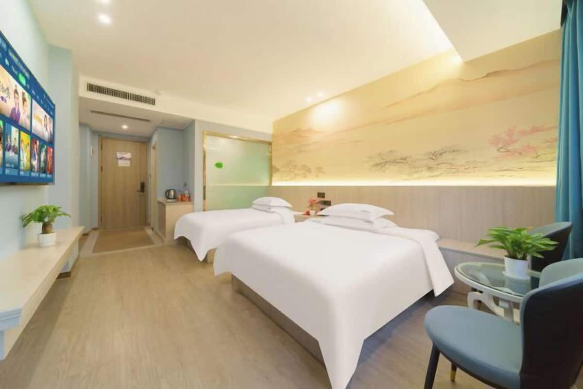 A hotel room with two beds, a desk, a chair, and a wall-mounted TV.
