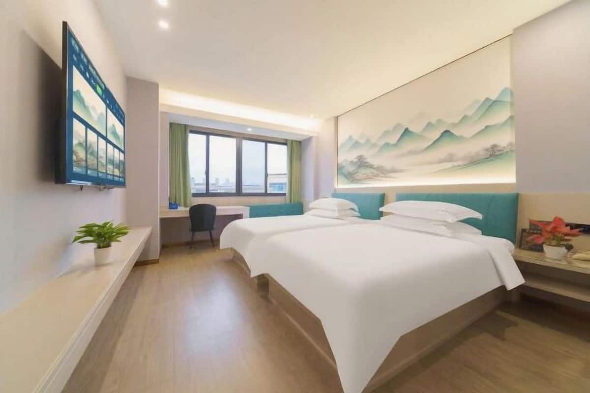 A hotel room with a bed, a desk, a chair, a TV, and a painting on the wall.