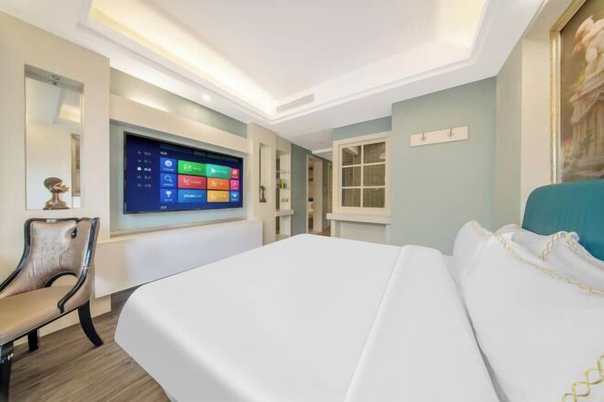 A hotel room with a bed, a TV mounted on the wall, a chair, and a window.