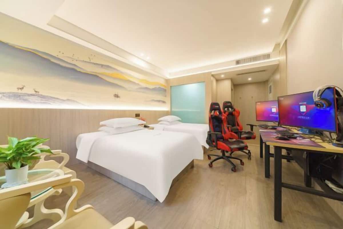 A hotel room with a bed, two chairs, a desk with a computer, and a wall mural.