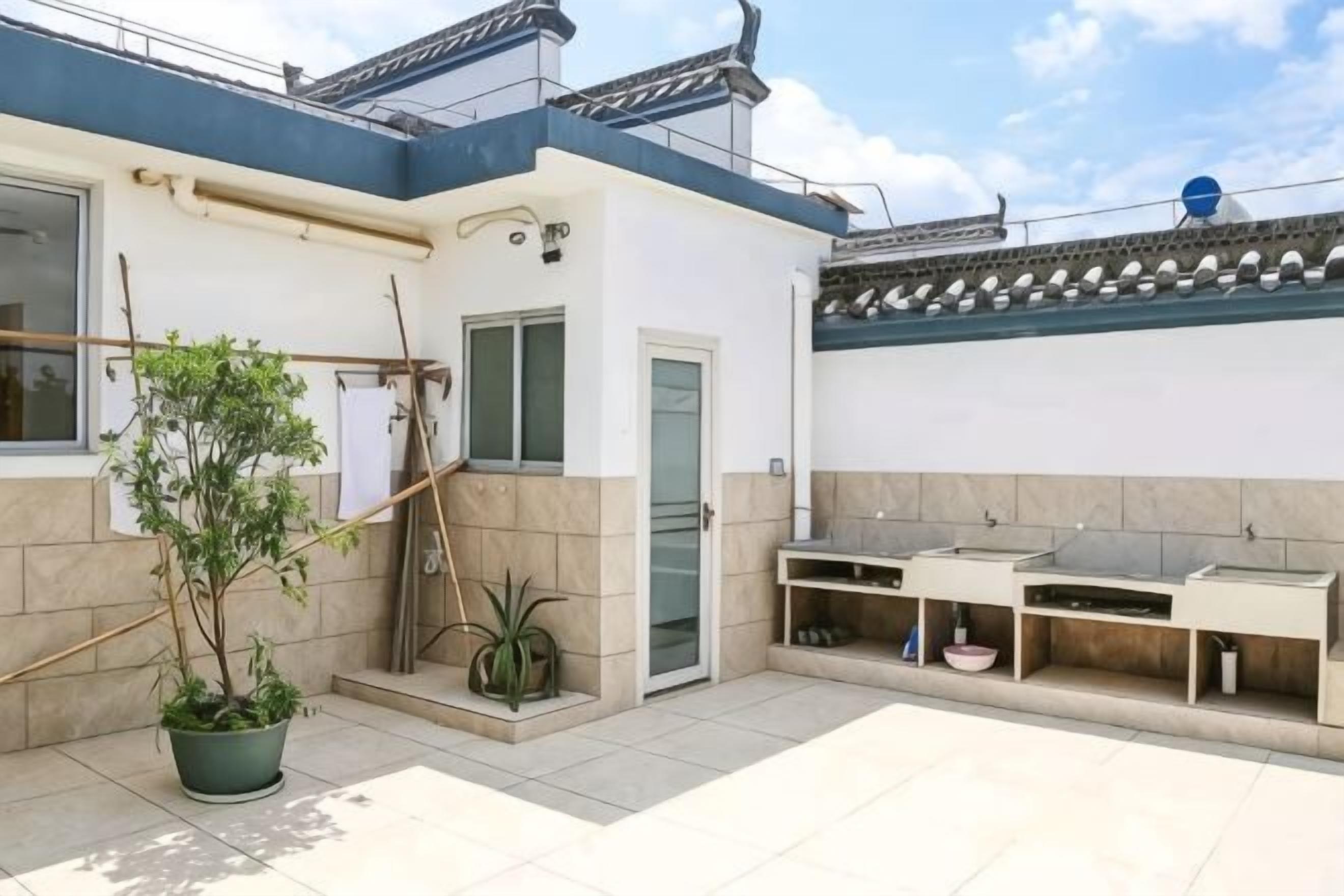 Een woongebouw met een betegeld terras, een deur, een kleine tuin met planten in potten en een traditioneel pannendak.