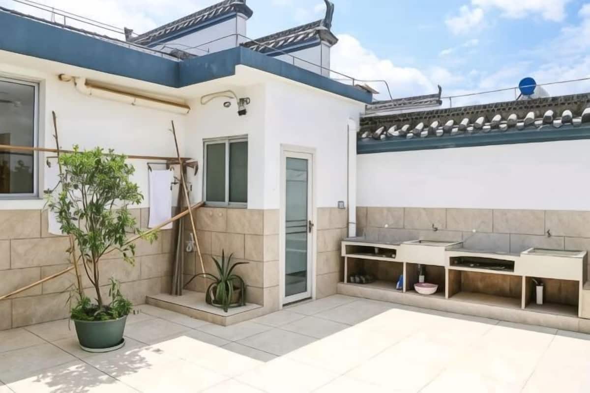 A residential building with a tiled patio, a door, a small garden with potted plants, and a traditional tiled roof.