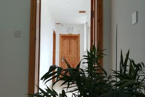 A hallway with a wooden door at the end, a plant in the foreground, and a white wall. - Huishu Renjia Chinese Inn (Wuyuan County Cultural Square Xiangao Ancient City) (Wuyuan)