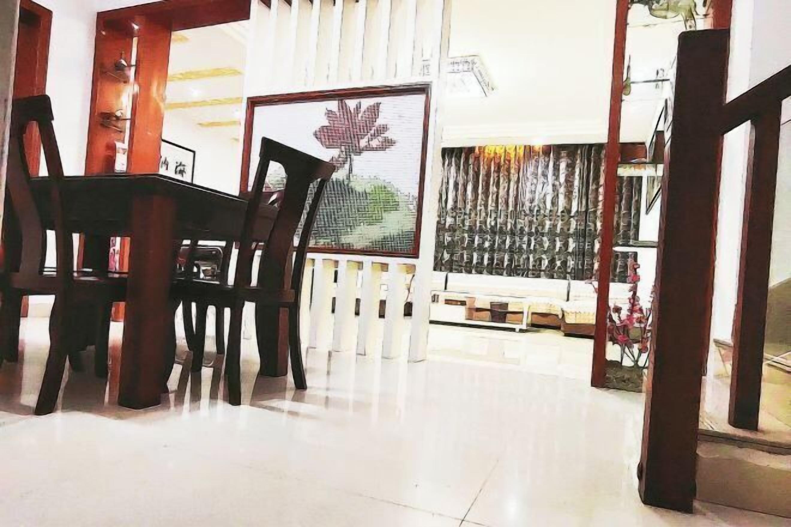 Un comedor con mesa y sillas de madera, un separador blanco con un cuadro enmarcado y un papel tapiz estampado.
