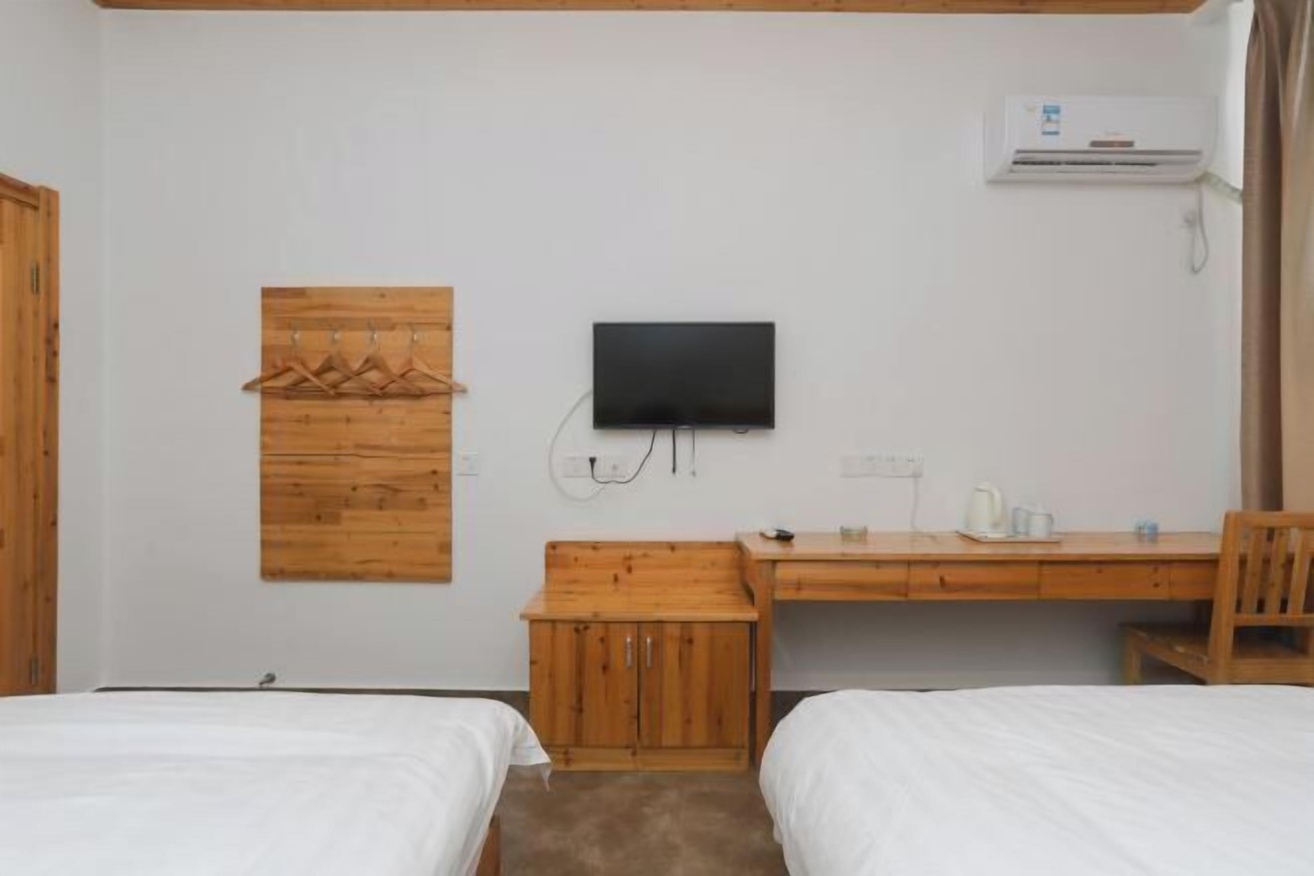 A hotel room with two beds, a wooden desk, a television, and an air conditioning unit.