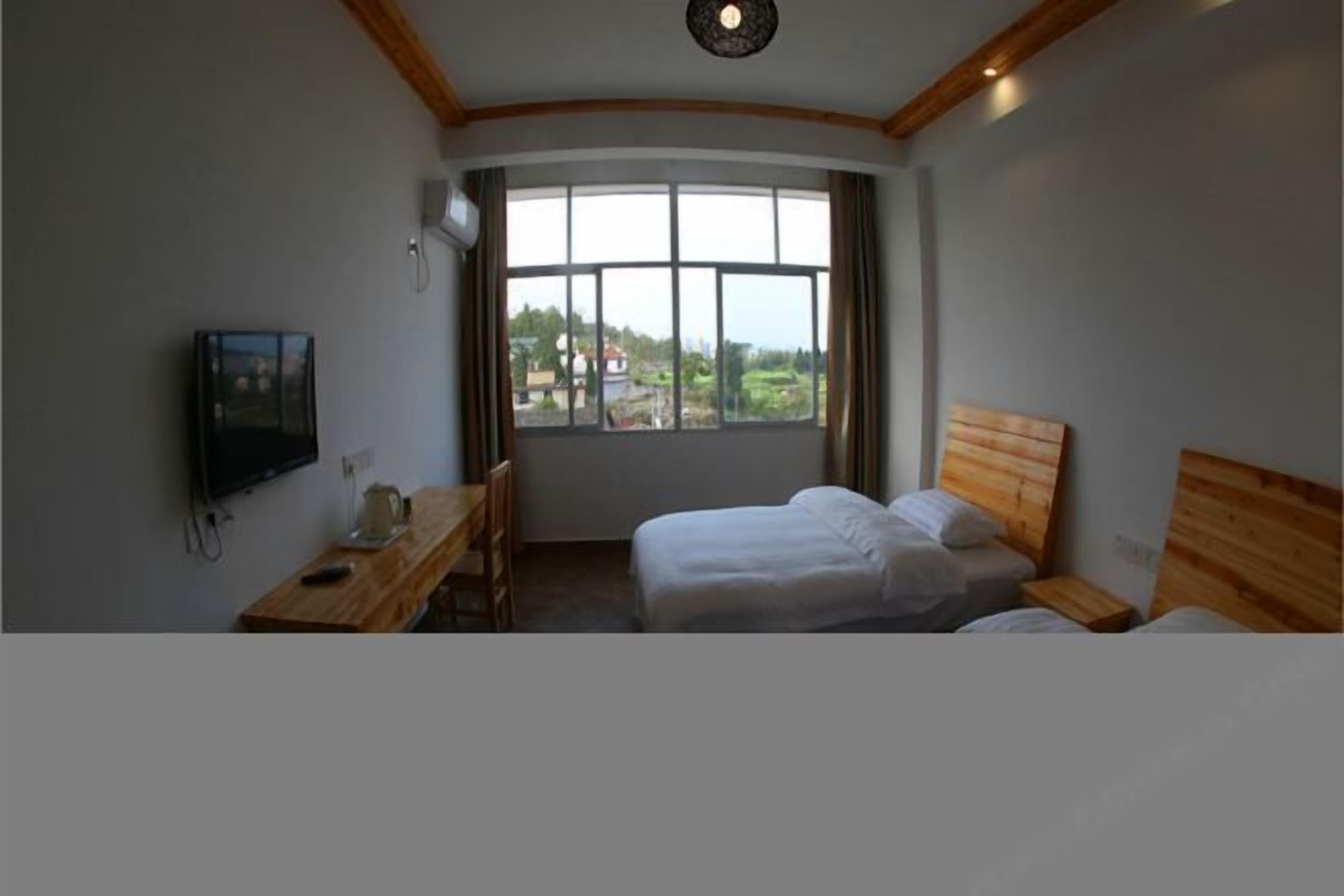 A hotel room with a large window, a desk with a chair, and two beds.