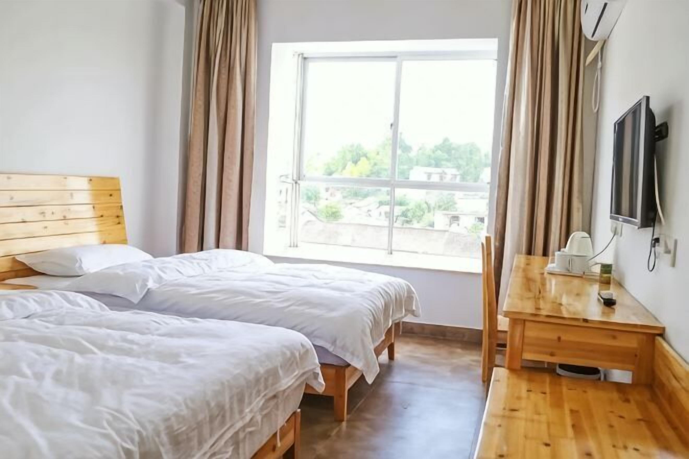 Una habitación con dos camas, una mesa de madera, un televisor y una ventana con cortinas.