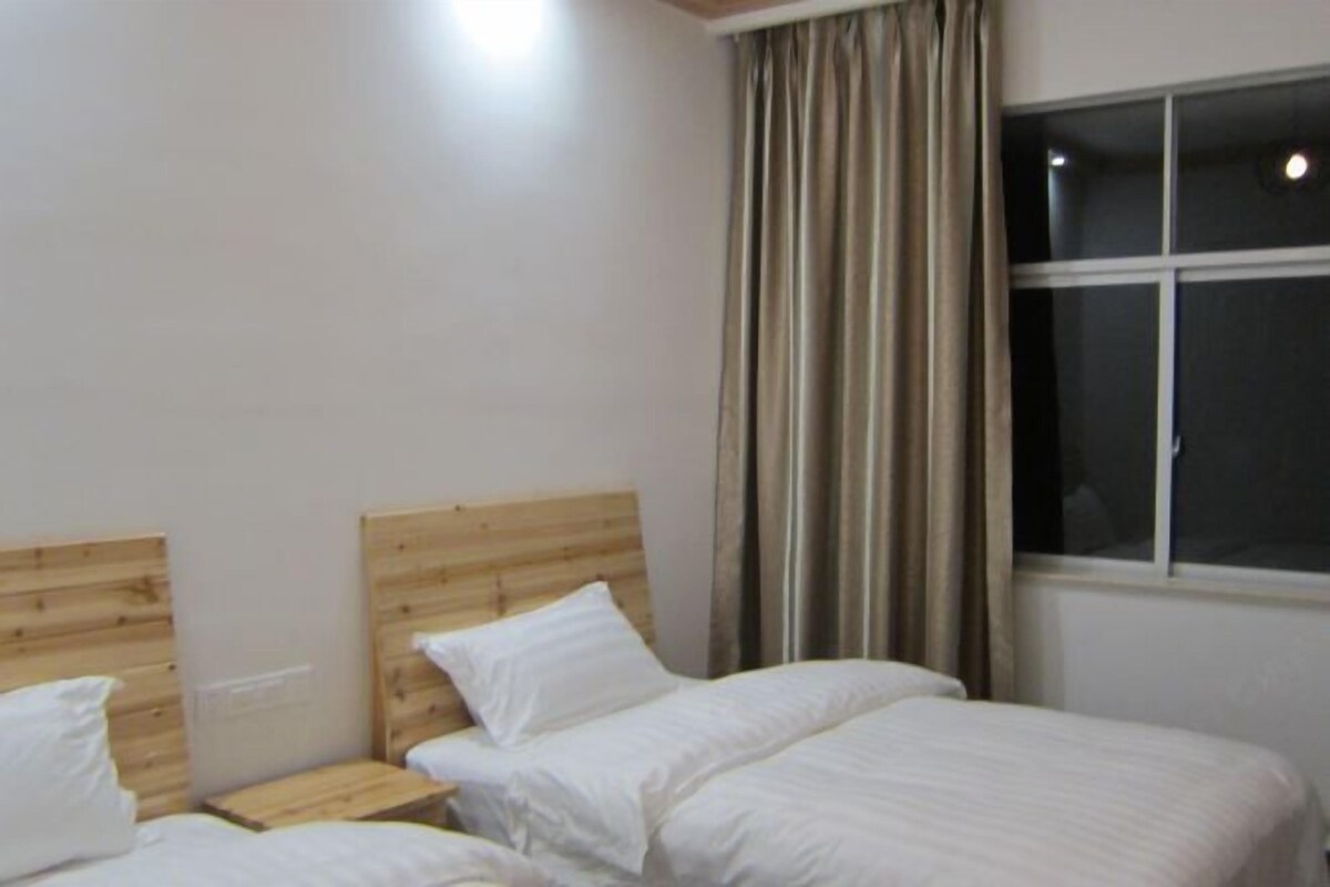 A room with two beds, wooden headboards, a window with curtains, and a night light.