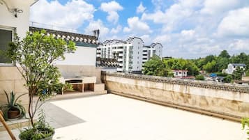 A rooftop terrace with potted plants, a tiled floor, and a view of residential buildings in the background.