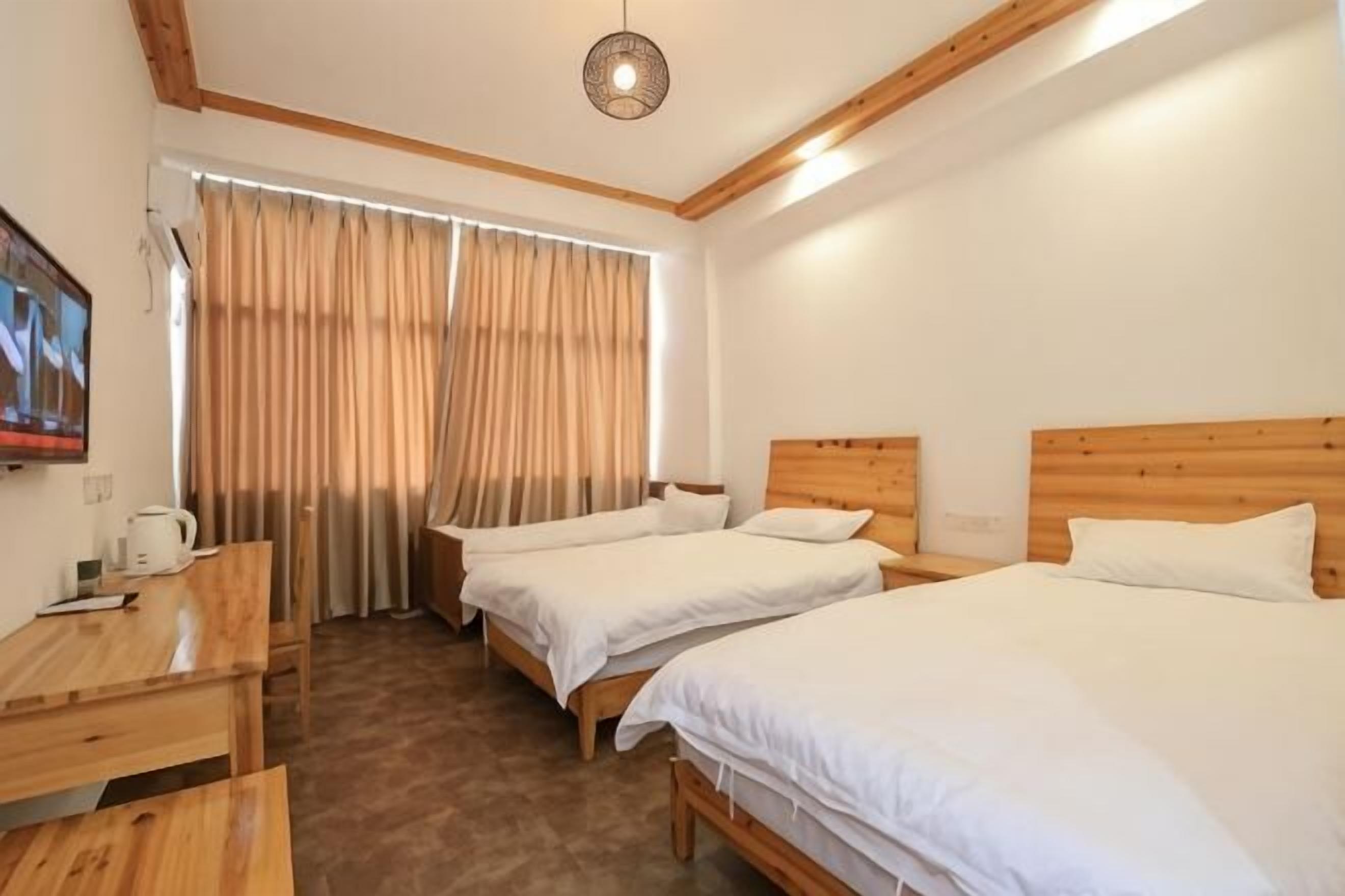 Habitación de hotel con dos camas, un escritorio, un televisor y una ventana con cortinas.
