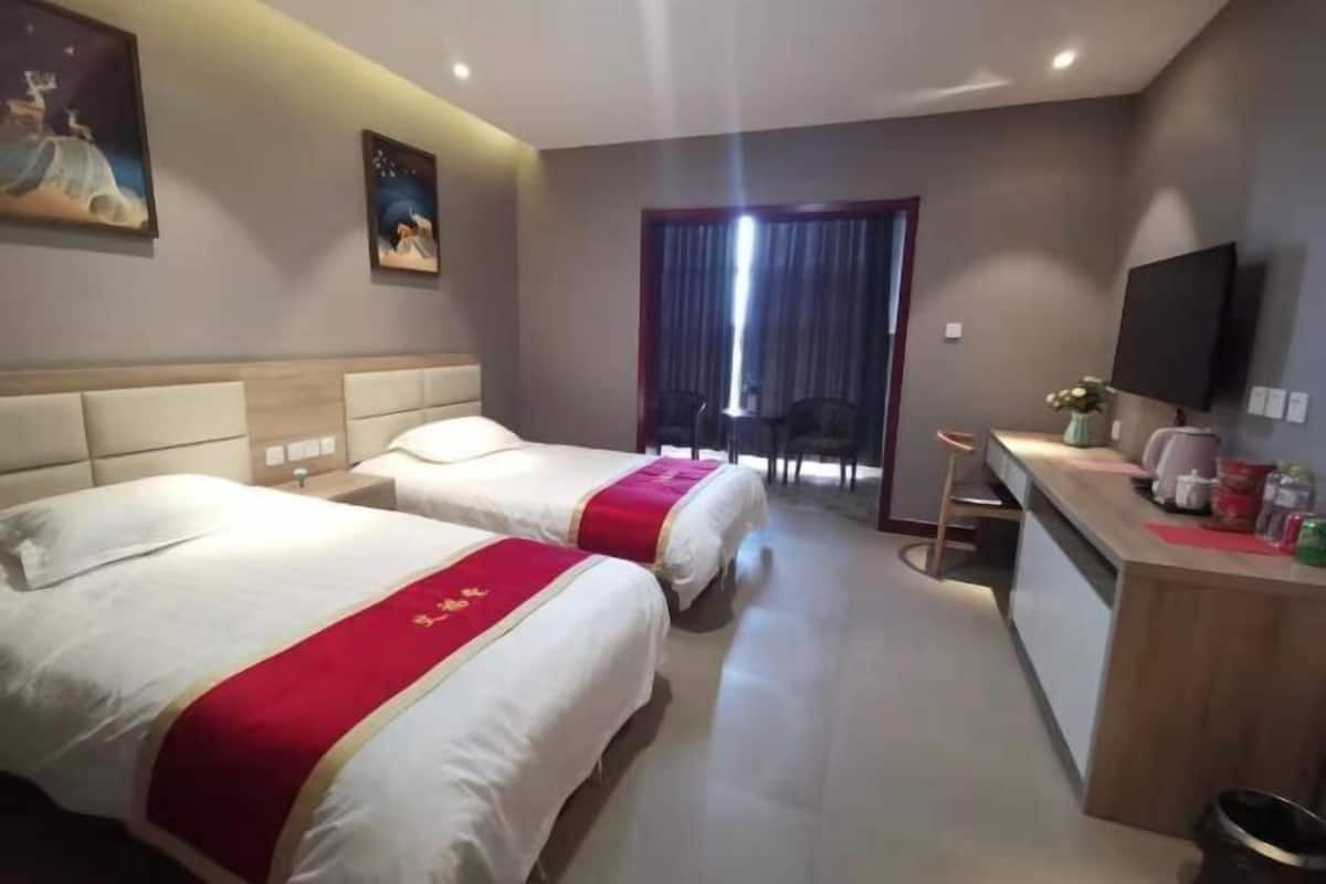 Ein Hotelzimmer mit zwei Betten, einem Schreibtisch mit Stuhl, einem Fernseher und einem Fenster mit Vorhängen.