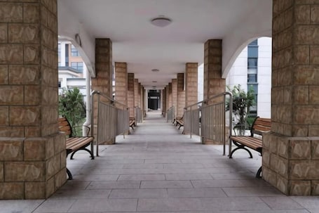A covered corridor with stone columns, benches, and a view of buildings in the distance.. Aifutang Grand Hotel
