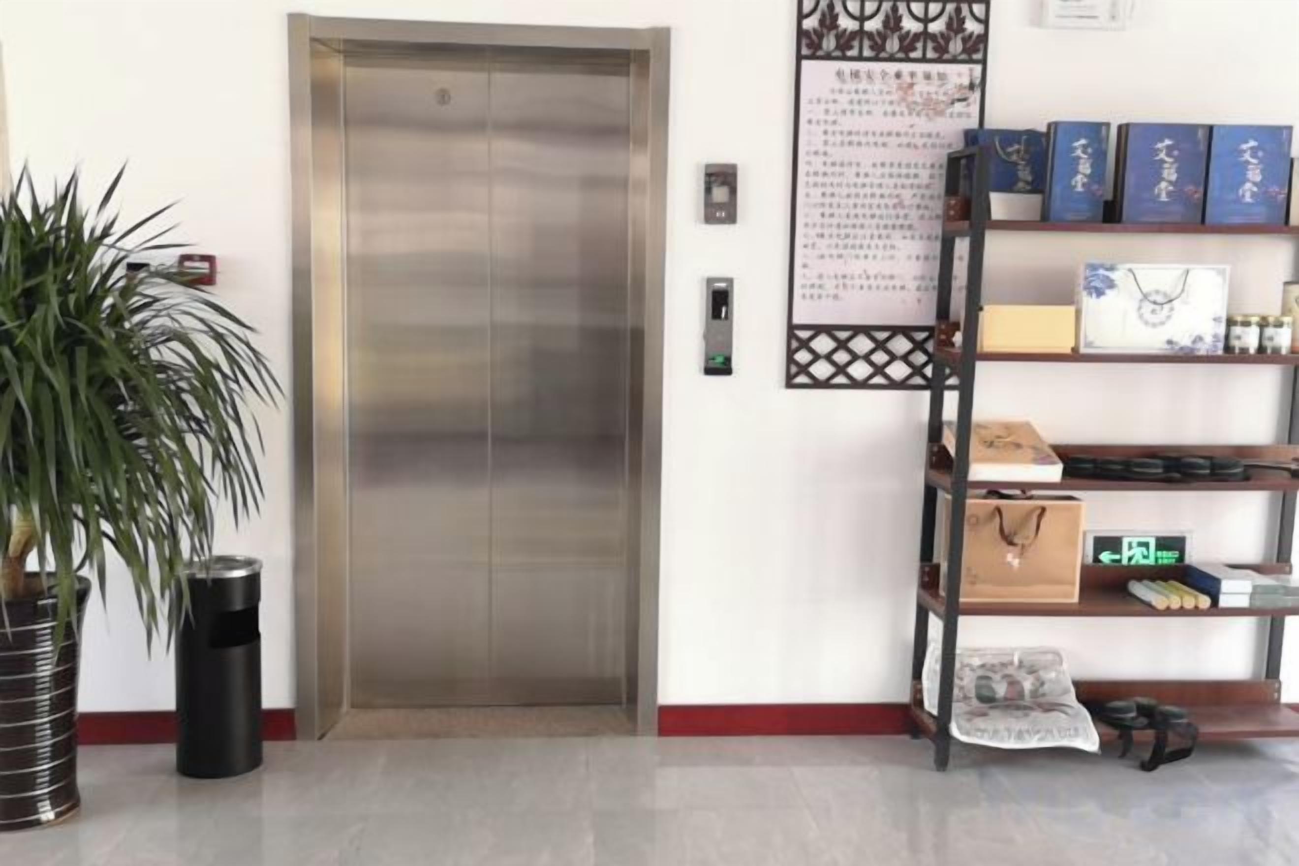 An elevator, a potted plant, a trash bin, a shelf with items, and a wall with a poster.