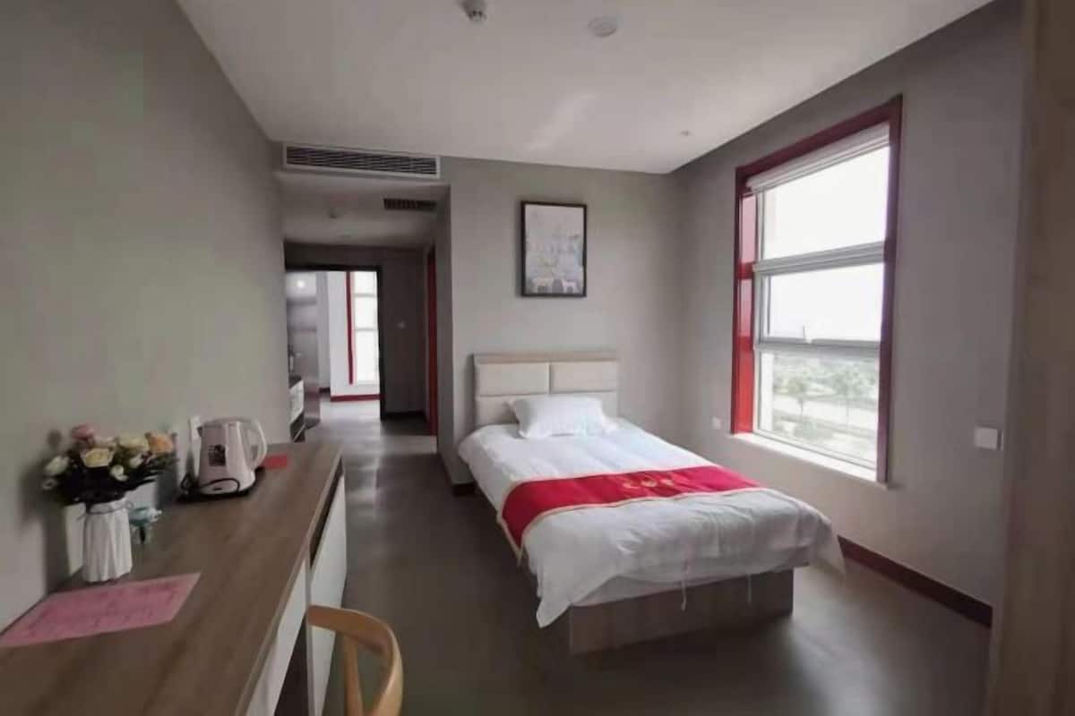 Ein Hotelzimmer mit Bett, Schreibtisch, Stuhl, Fenster und einem Bild an der Wand.