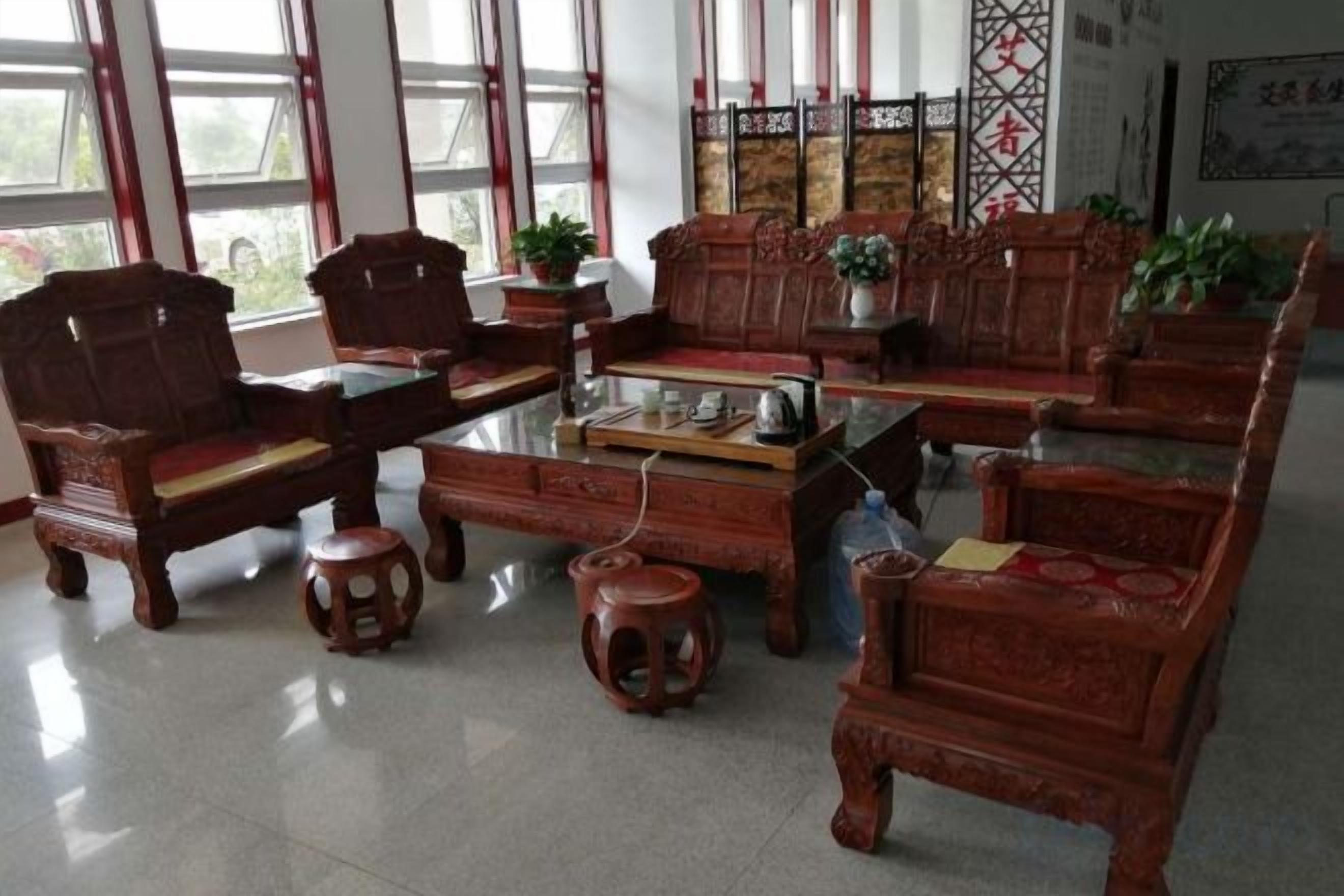 A traditional wooden furniture arrangement with a glass-top coffee table, multiple chairs, and stools.