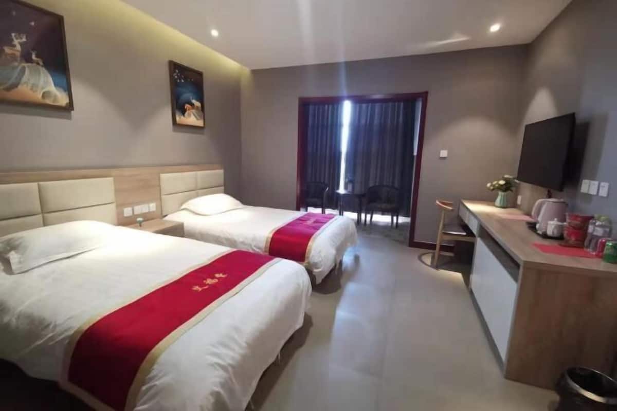 Ein Hotelzimmer mit zwei Betten, einem Schreibtisch mit Stuhl, einem Fernseher und einem Fenster mit Vorhängen.