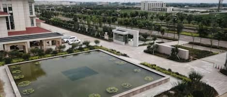 A large rectangular pool with lily pads, surrounded by a landscaped garden and a building with a red roof.
