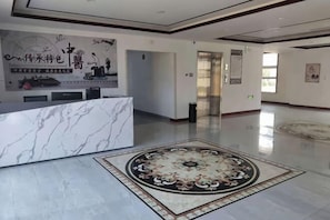 Un vestíbulo de hotel con una recepción de mármol, una alfombra estampada y una pared con detalles decorativos.
