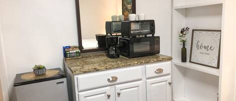 Una kitchenette equipada con cafetera, microondas y refrigerador pequeño.