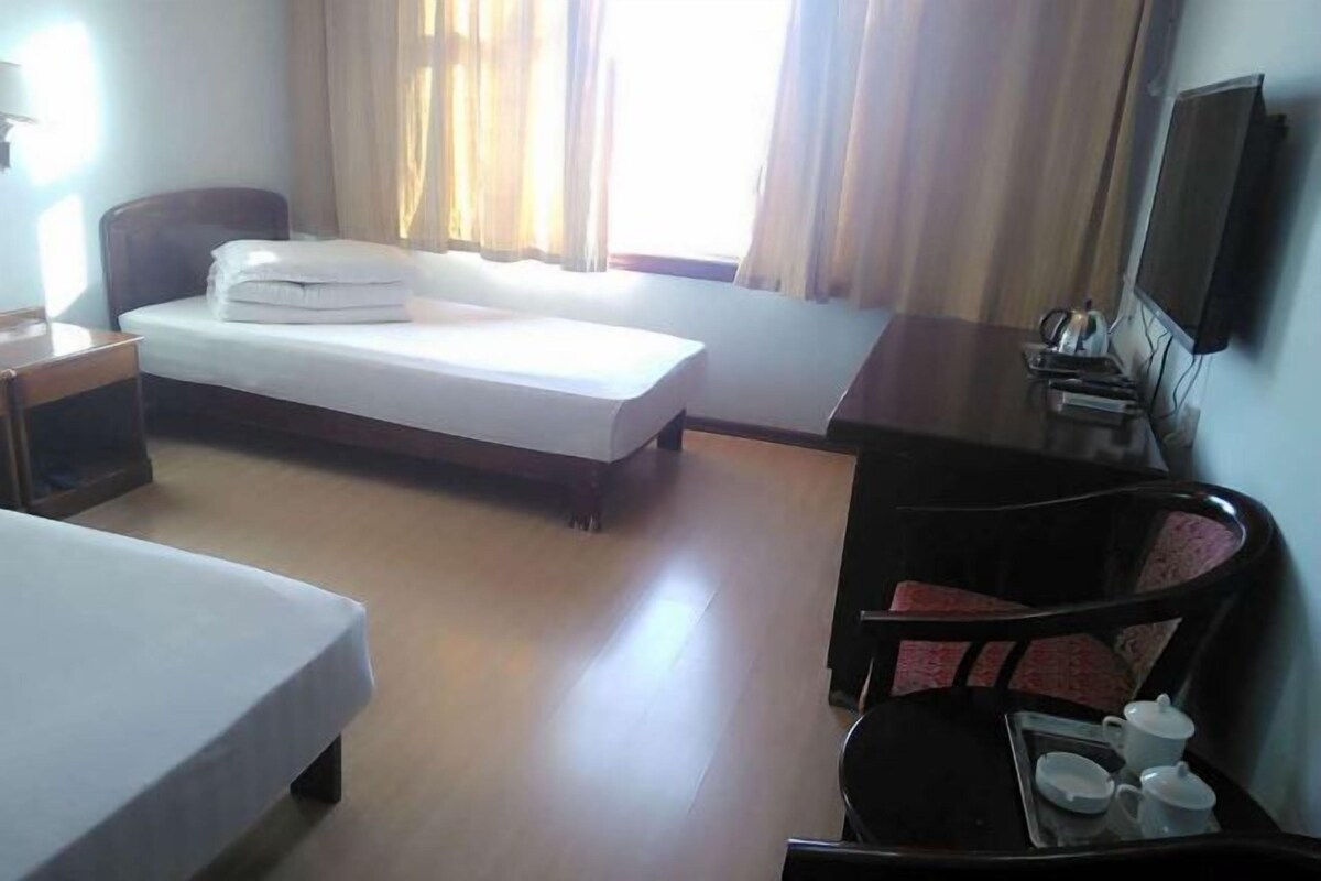 Habitación de hotel con cama, escritorio, silla, televisor y ventana con cortinas.