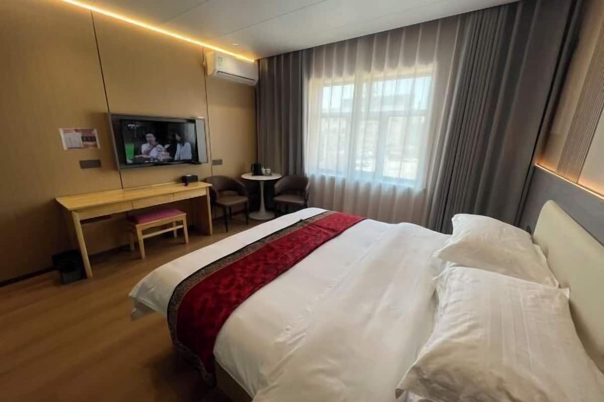 A hotel room with a bed, a desk, a chair, a television, and a window with curtains.